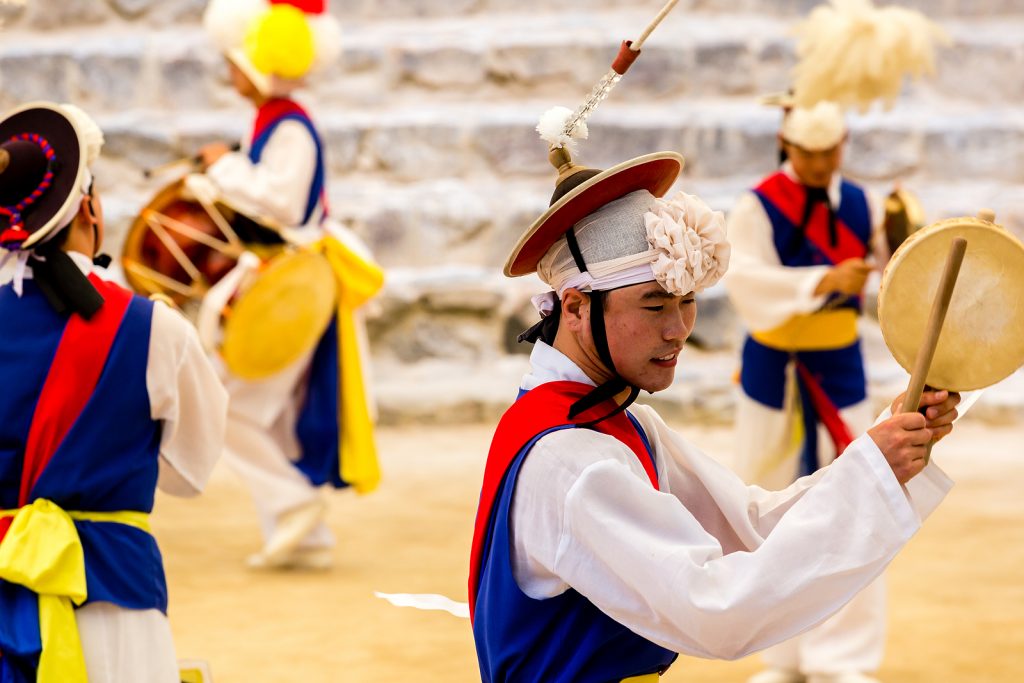 A group fo male dancers dancing and playing traditional Korean instrument